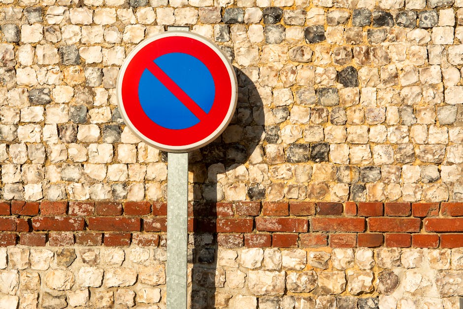 A round traffic sign with a white background, a bold black letter 'P', and a red diagonal line crossing through it, indicating no parking. The sign is mounted on a metal pole positioned in an outdoor area under an overcast sky. The background shows a grey sky with no other visible structures. This sign is relevant to road closure and temporary parking rules for Northolt moves, as noted on the webpage about house removals and relocation services by Man with Van Northolt. The sign may influence vehicular access during the home relocation and furniture transport process, which involves loading and unloading household items, such as cardboard boxes, packing materials, and furniture, at the property and loading area visible in the context of moving logistics.